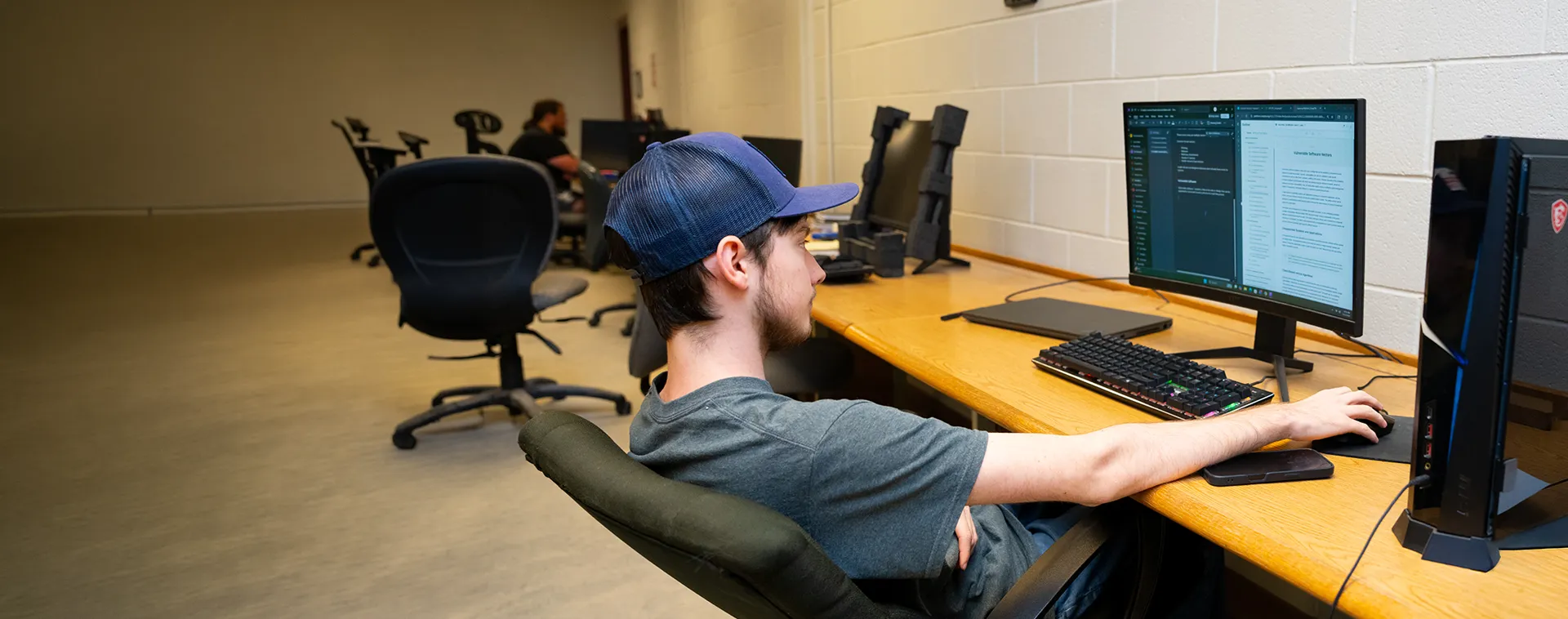 Person seated at desktop computer typing on keyboard in classroom lab with multiple monitors and chairs