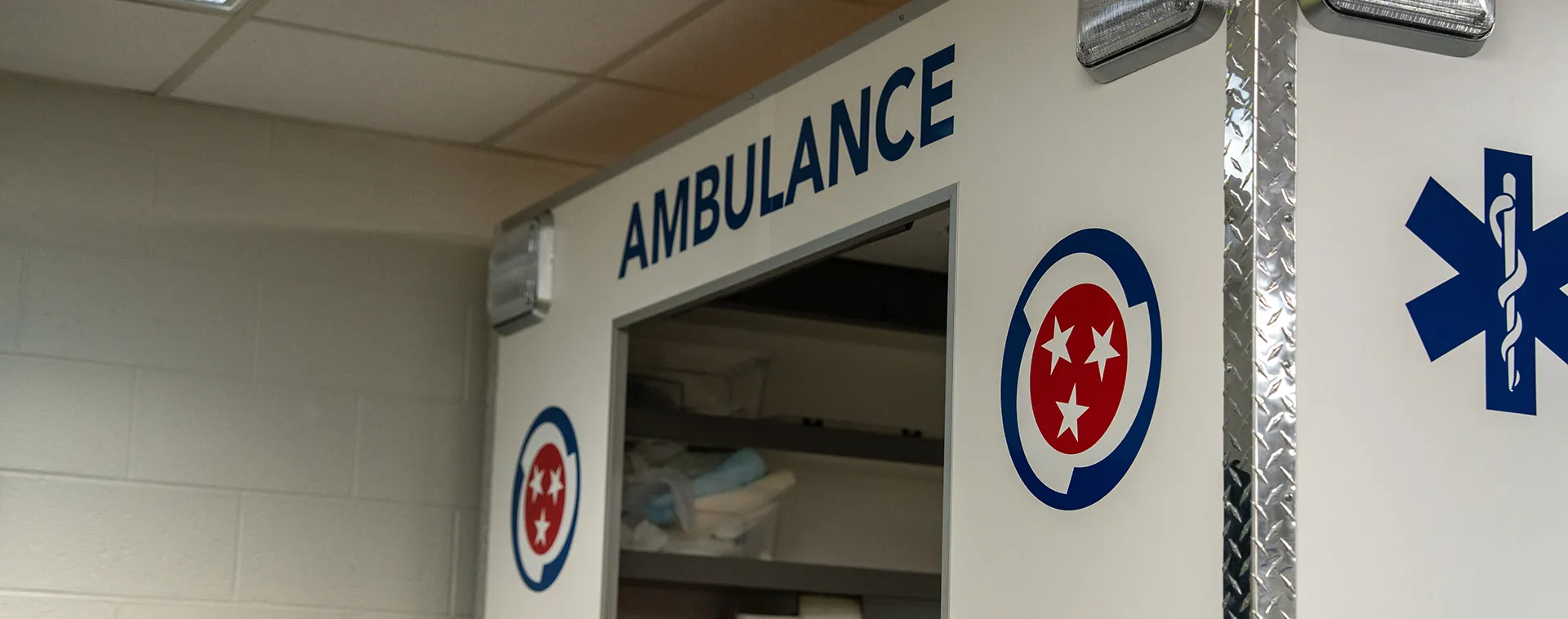 Ambulance training unit with &ldquo;AMBULANCE&rdquo; text and Tennessee logo on white panel inside classroom.