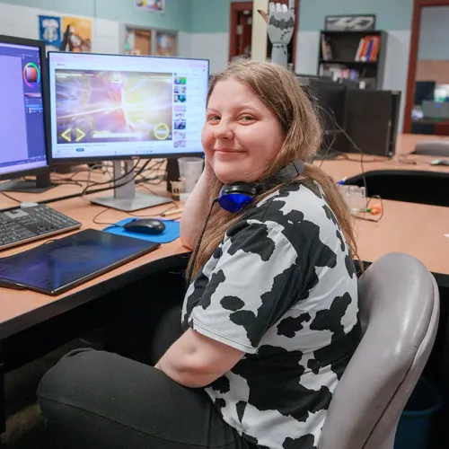 Person seated at workstation with headphones around neck, editing on screen with drawing tablet in classroom