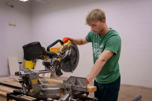 Person operating a miter saw cutting a wood board on a workbench in a workshop